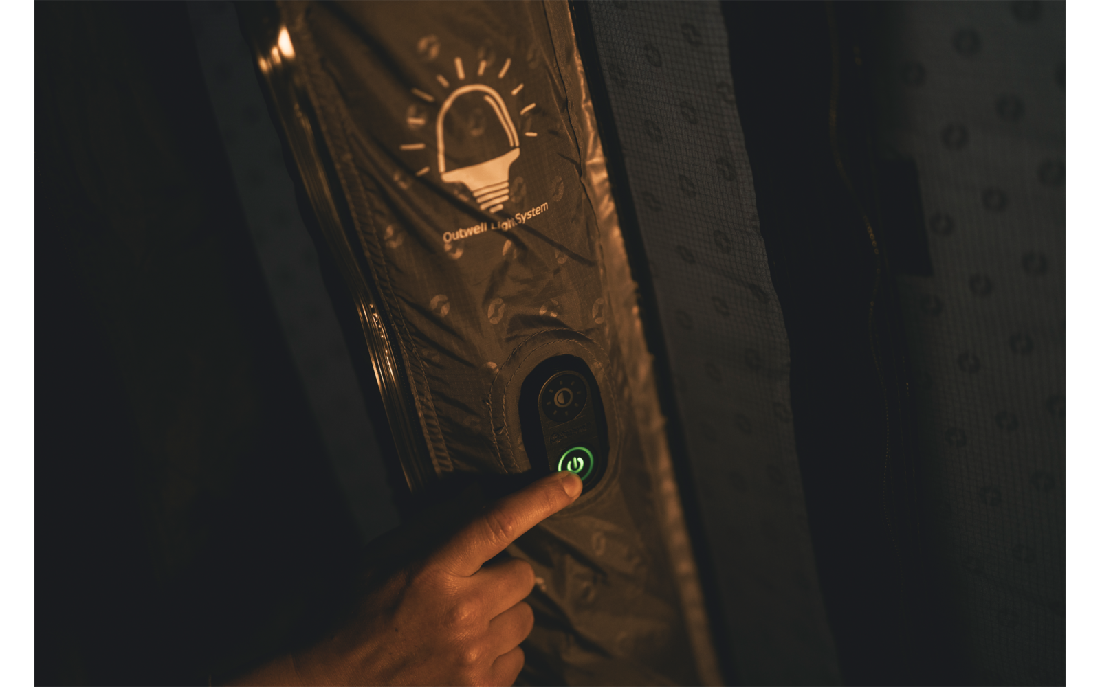 Hand drückt einen grün leuchtenden runden Knopf auf einem vertikalen Panel, darüber ein Glühbirnen-Symbol