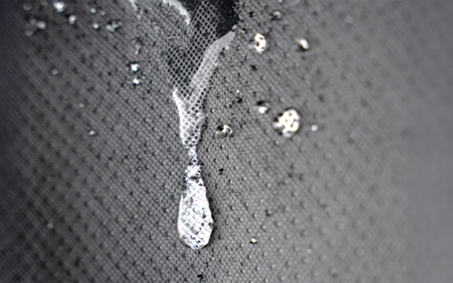 Gota transparente y pequeñas salpicaduras sobre una superficie gris texturizada