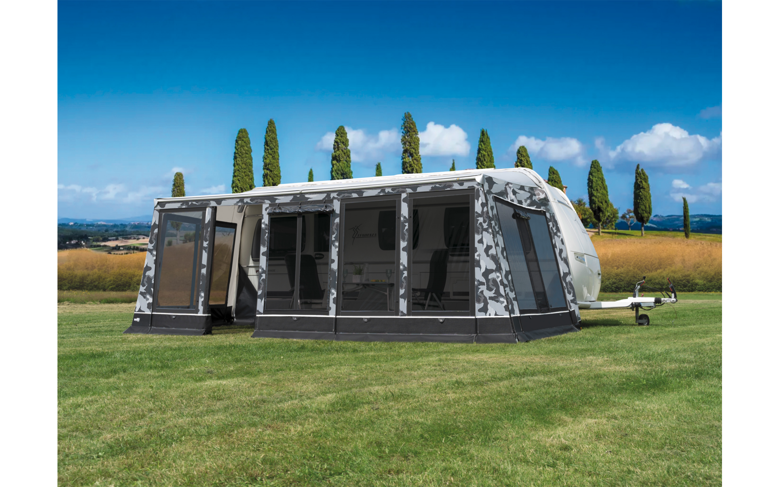 Grote grijs-witte voortent van een caravan op een groen grasveld met bomen op de achtergrond