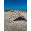 Dreieckiges Sonnensegel mit braun-beigem Muster auf sandigem Strand, Metallstangen, Dünen mit Strandgras und blauem Himmel im Hintergrund