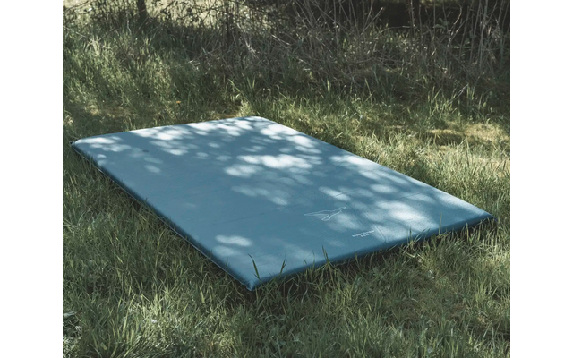 Eine weiße rechteckige Fläche liegt auf dem Gras, umgeben von Bäumen und Schatten