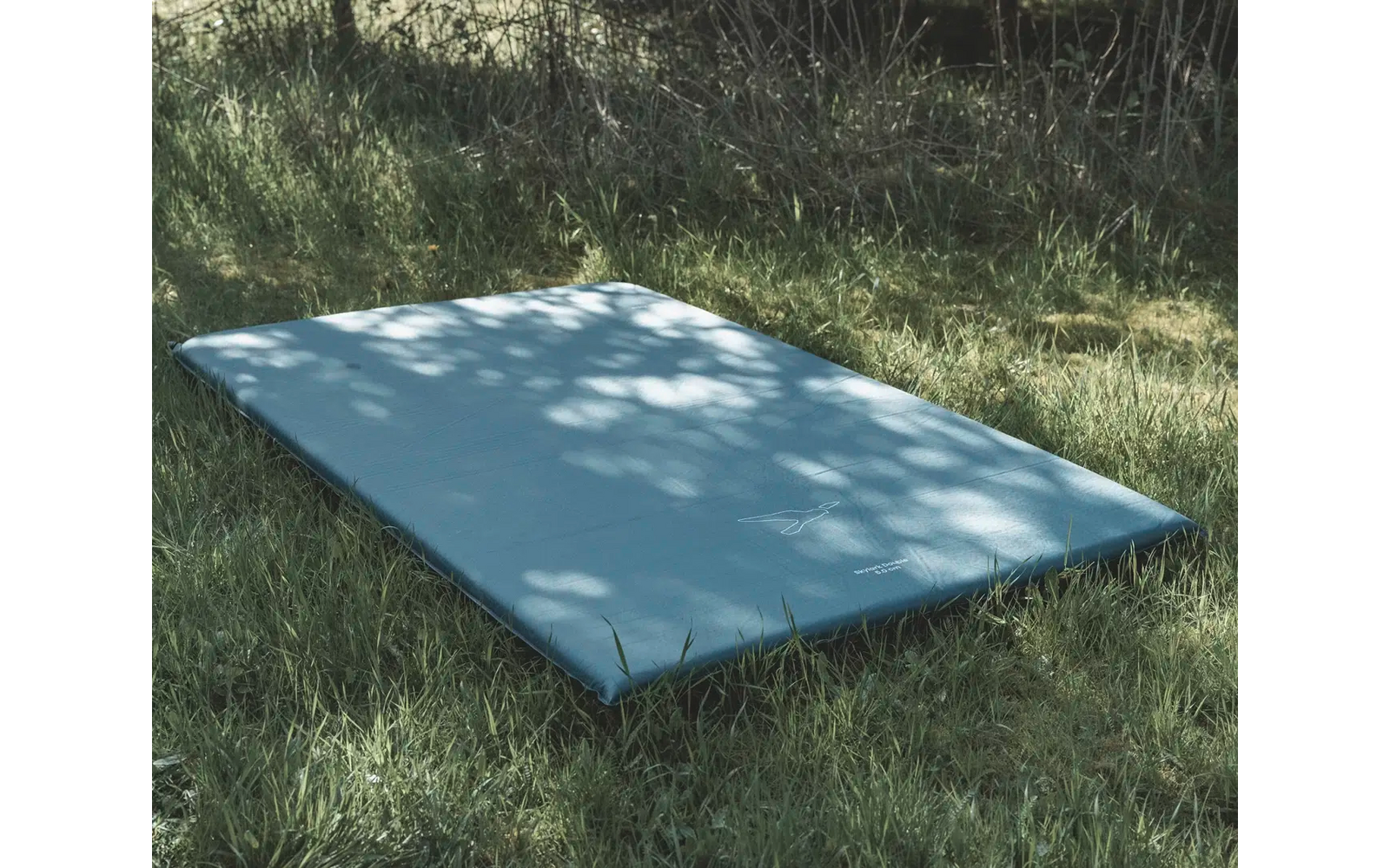 Eine weiße rechteckige Fläche liegt auf dem Gras, umgeben von Bäumen und Schatten