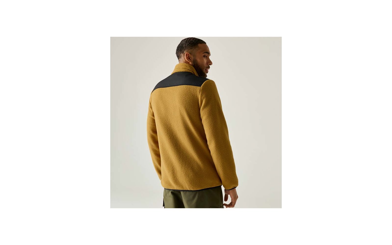 Rückansicht eines Mannes in senfgelber Fleecejacke mit schwarzem Schulterbereich und olivgrünen Hosen