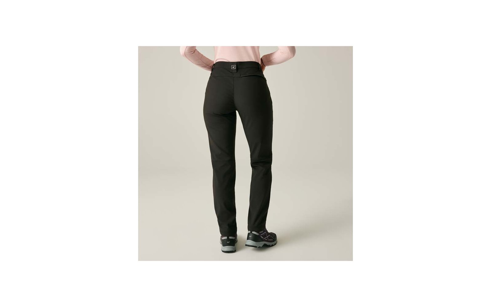Achteraanzicht van een persoon met een zwarte broek, roze bovenstuk en zwarte sportschoenen