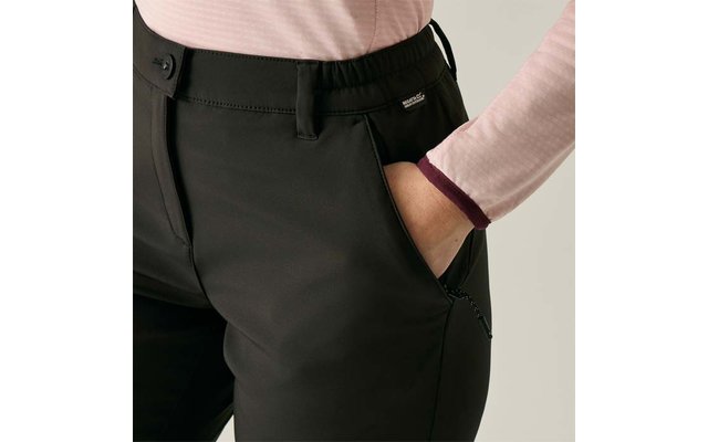 Onderlichaam van een persoon in zwarte broek, rechterhand in de voorzak, lichtroze top met lange mouwen en donker boord, zichtbare riemlussen en klein logo bij de zak