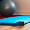 Blauwe yogamat en grijze fitnessbal voor witte muur