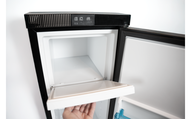 Schwarzer Mini-Kühlschrank, geöffnete Tür, leeres weißes Innenfach, Hand zieht ein herausnehmbares Fach heraus