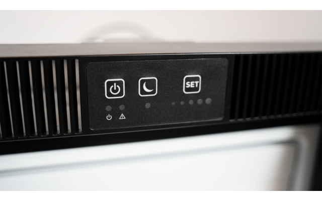 Nahaufnahme eines schwarzen Bedienfelds mit drei Tasten: Ein-/Aus-Symbol, Mondsymbol und "SET". Unter den Tasten fünf kleine LED-Punkte und drei kleine Symbole. Vertikale Lüftungsschlitze links und rechts, darunter weiße Fläche