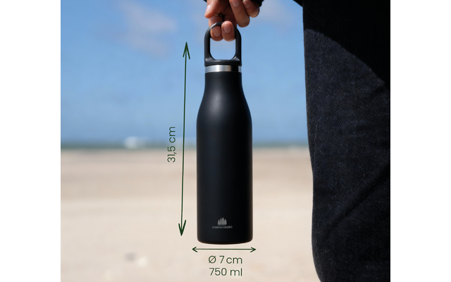 Hand hält schwarze Trinkflasche mit Tragegriff; grüne Pfeile und Beschriftungen '31,5 cm', 'Ø 7 cm' und '750 ml'; Sandstrand und Himmel im Hintergrund; Teil eines schwarzen Kleidungsstücks sichtbar