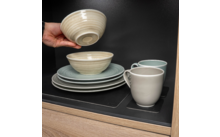 Une main pose un bol beige sur une pile d'assiettes et de tasses dans un placard