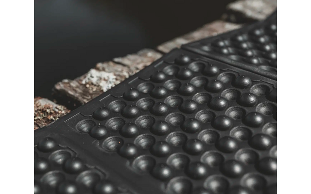 Nahaufnahme einer schwarzen, gummierten Oberfläche mit runden Erhebungen und einem angrenzenden, metallischen Streifen mit Schrauben