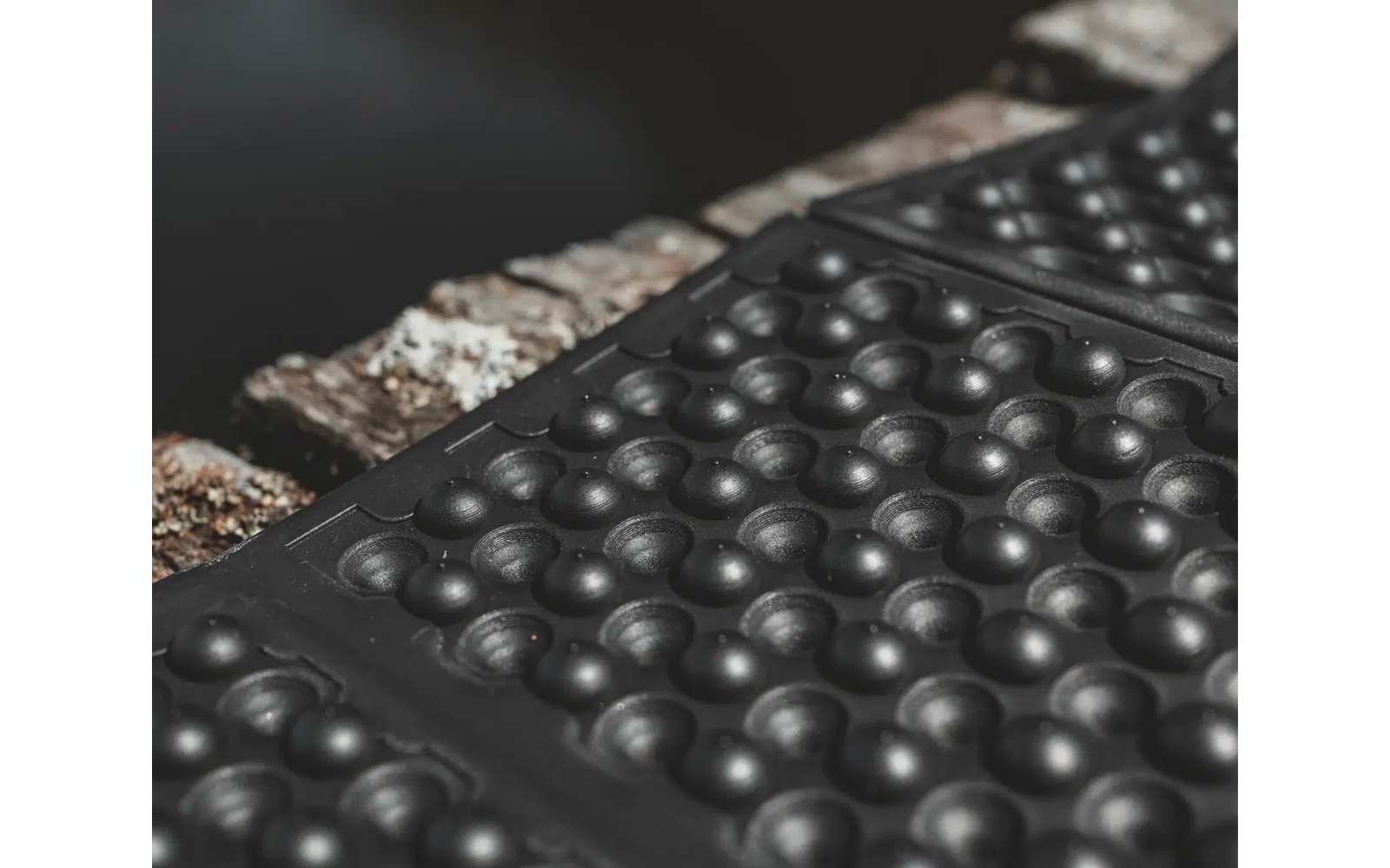 Nahaufnahme einer schwarzen, gummierten Oberfläche mit runden Erhebungen und einem angrenzenden, metallischen Streifen mit Schrauben