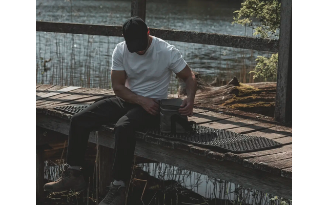 Mann sitzt auf einem Steg am Wasser und blickt auf sein Handy