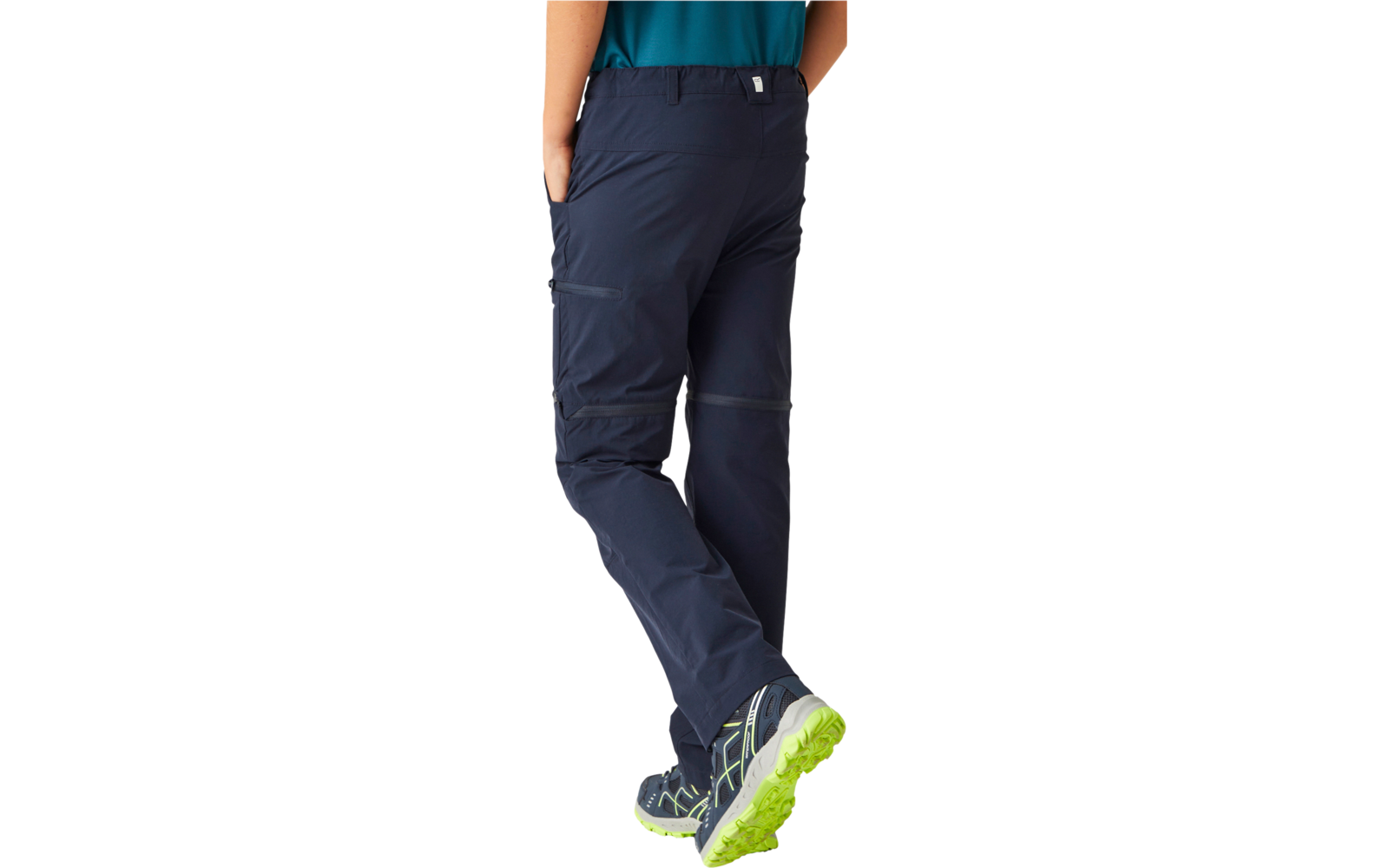 Rear view of a person from the hips down wearing dark blue outdoor trousers, edge of a turquoise top visible, gray hiking shoes with bright green soles, left hand in back pocket