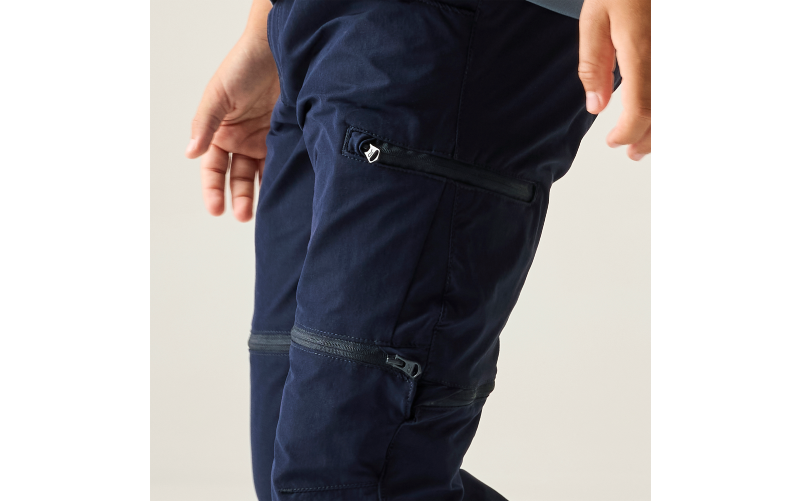 Close-up of navy blue cargo pants with multiple zippers; hands at the edges of the image