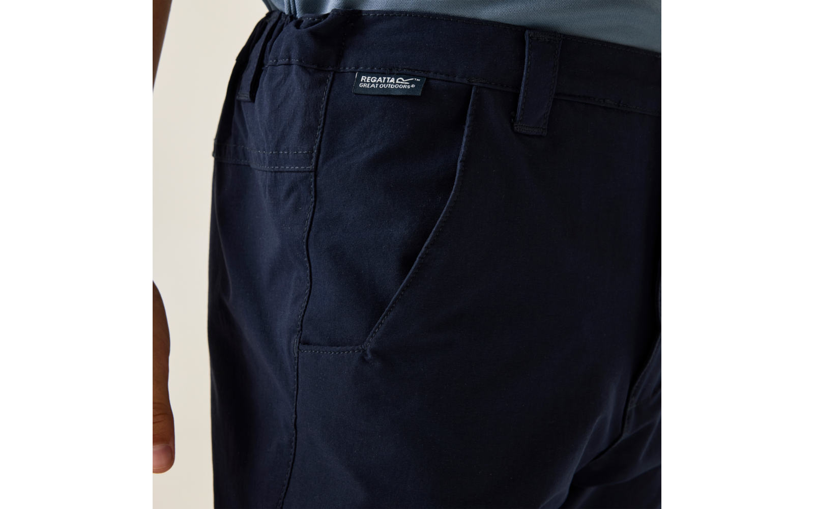 Close-up of a person's hip wearing dark blue trousers with a visible label and a partially visible left hand