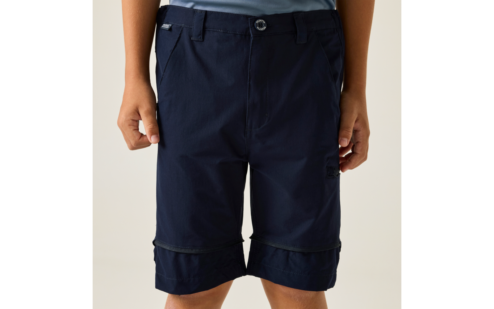 Lower torso of a person wearing dark blue knee-length shorts with a button, belt loops and side pockets; hands visible at the sides