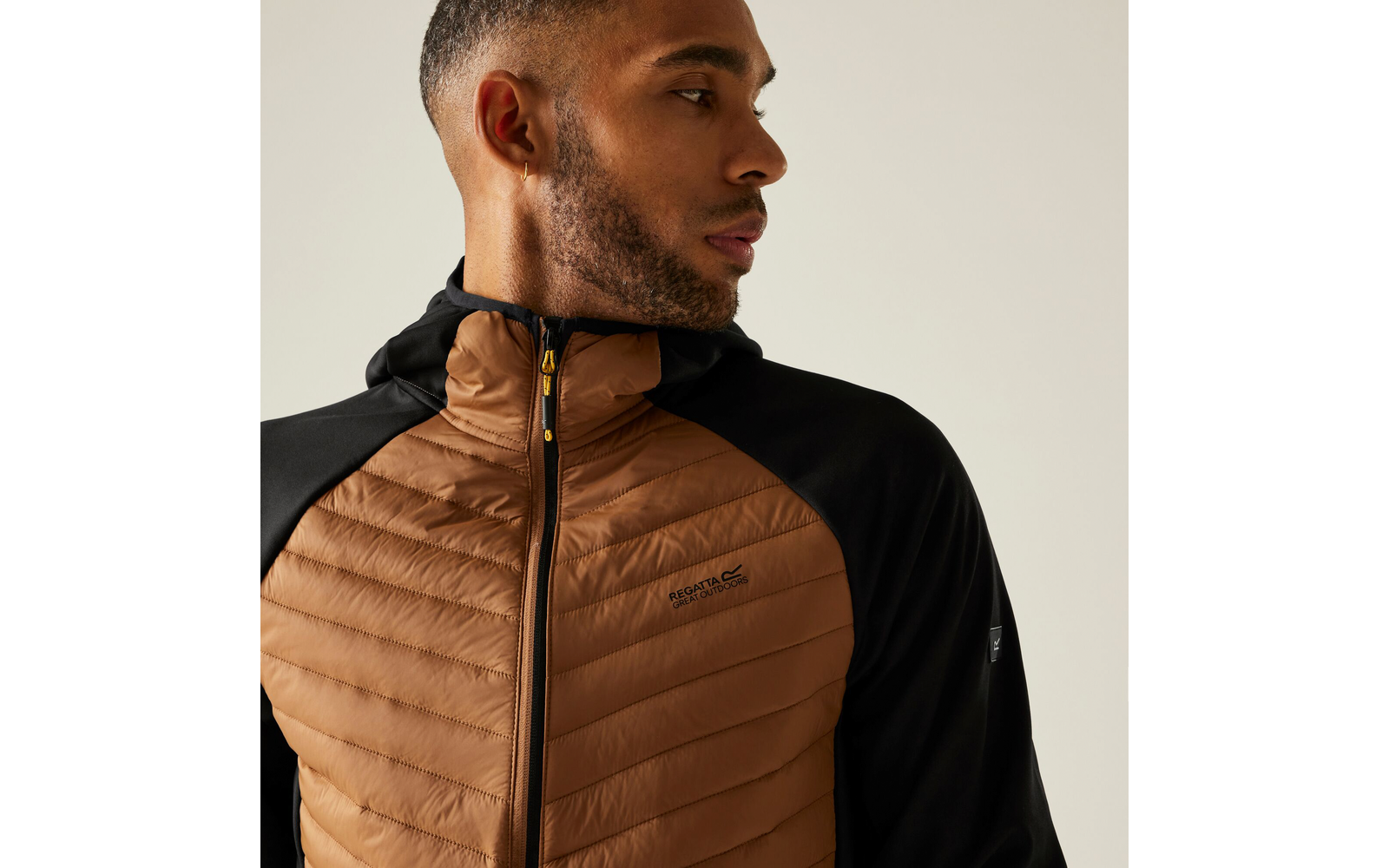 Porträt eines Mannes mit kurzem Bart, der eine braune gesteppte Jacke mit schwarzem Kragen trägt und nach links schaut