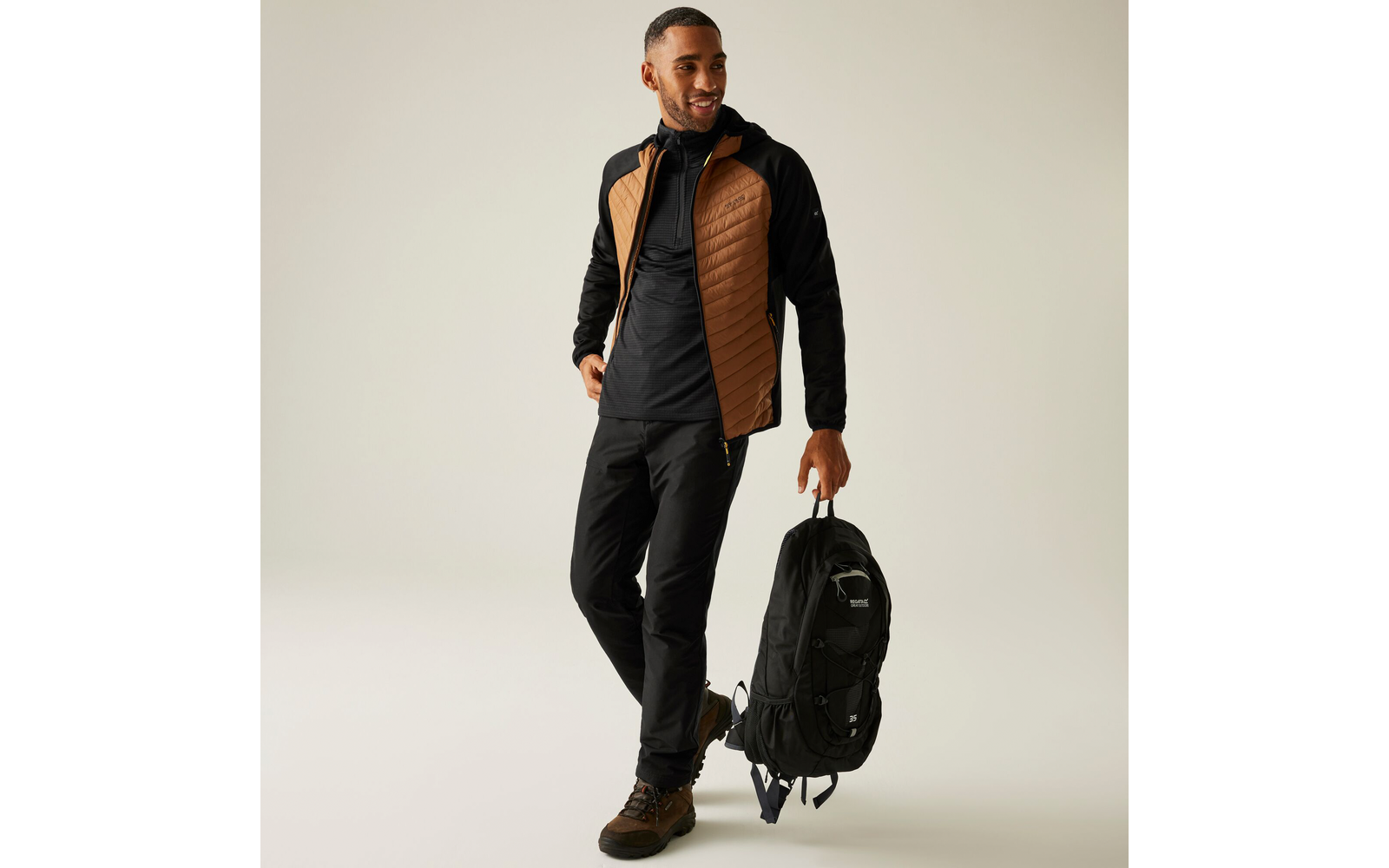 Mann in schwarzer Kleidung und brauner Weste mit schwarzem Rucksack in der Hand