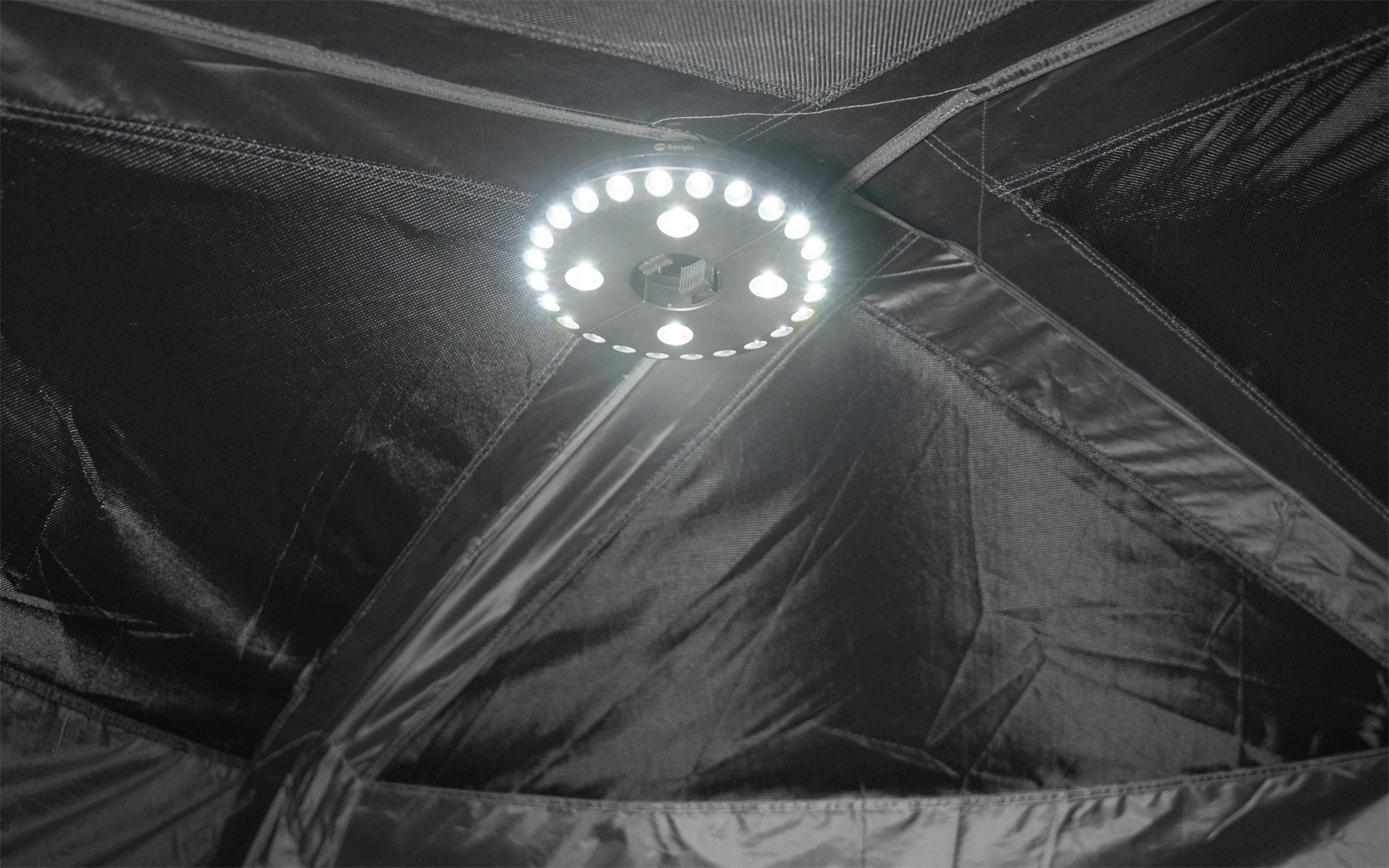 Kreisförmiger LED-Leuchtring in der Bildmitte, umgeben von schwarzen Stoffpaneelen mit sichtbaren Nähten