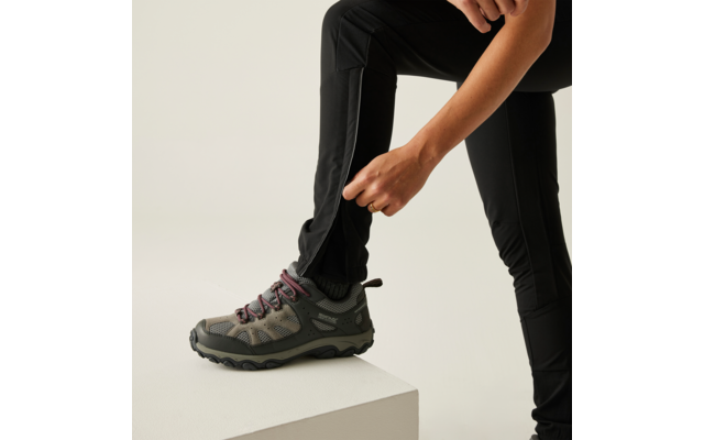Person zieht eine schwarze Socke über den linken Fuß, trägt schwarze Hose und graue Sportschuhe