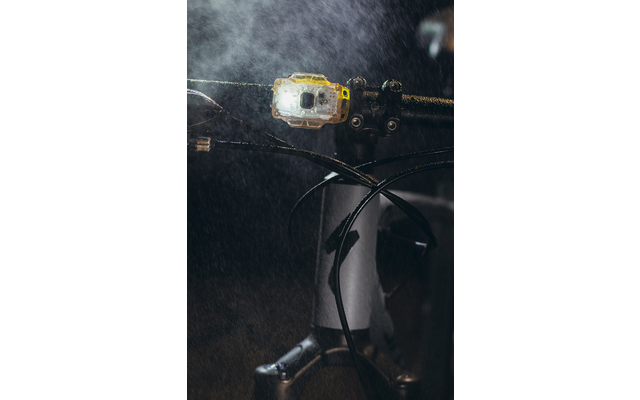 Nahaufnahme eines Fahrradlenkers mit eingeschalteter Lampe und Wassertröpfchen in der Luft