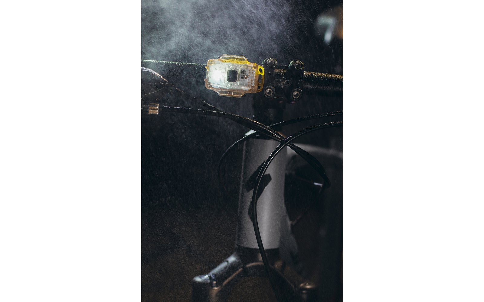 Nahaufnahme eines Fahrradlenkers mit eingeschalteter Lampe und Wassertröpfchen in der Luft