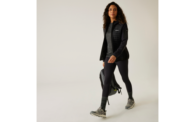 Femme vêtue de vêtements de sport noirs marchant devant un fond blanc