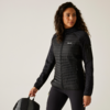 Femme aux cheveux bouclés portant une veste noire tenant une poignée de valise