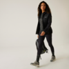 Femme vêtue de vêtements de sport noirs marchant devant un fond blanc