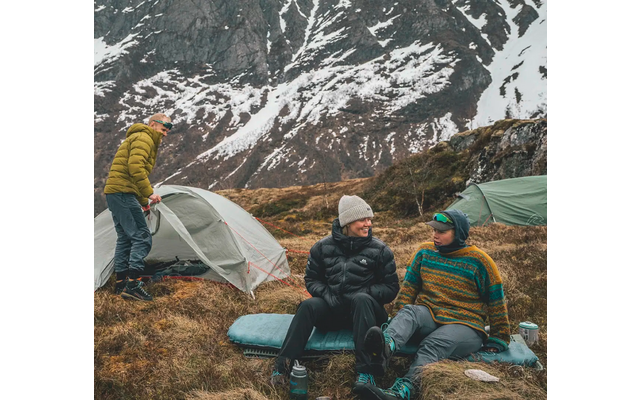 Drei Personen beim Camping in den Bergen mit Schnee im Hintergrund