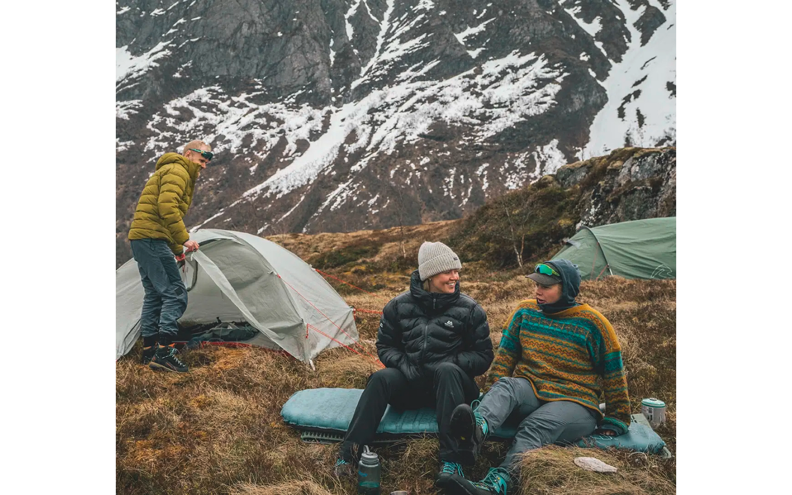 Drei Personen beim Camping in den Bergen mit Schnee im Hintergrund