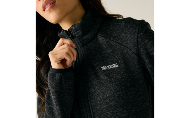 Person von Kinn bis Brust, Hand zieht Reißverschluss einer schwarzen, melierten Fleecejacke mit hohem Kragen und sichtbarem "Regatta Great Outdoors"-Logo auf der linken Brust