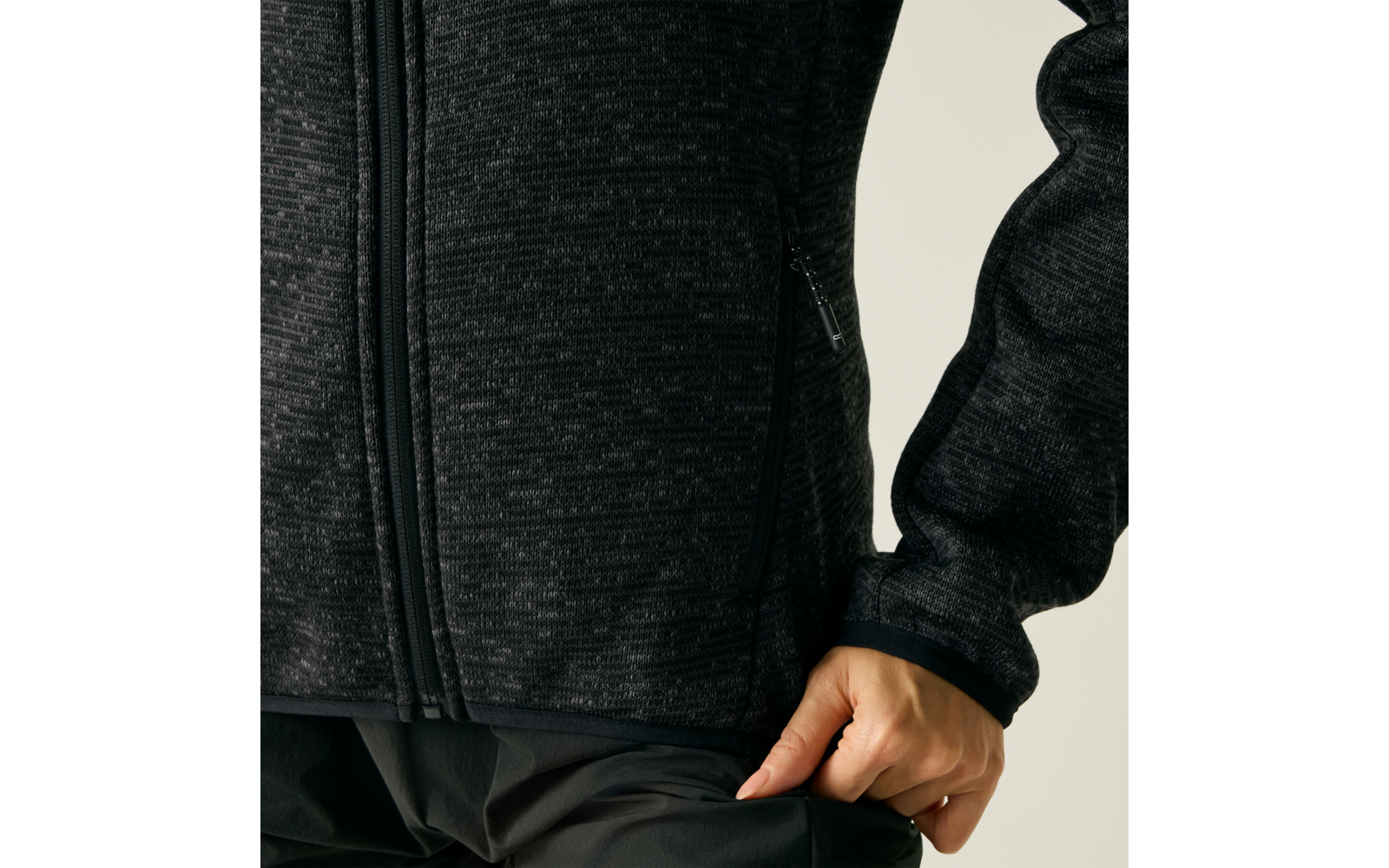 Nahaufnahme eines Oberkörpers in einer dunklen, melierten Jacke mit Reißverschluss; rechte Hand am Saum