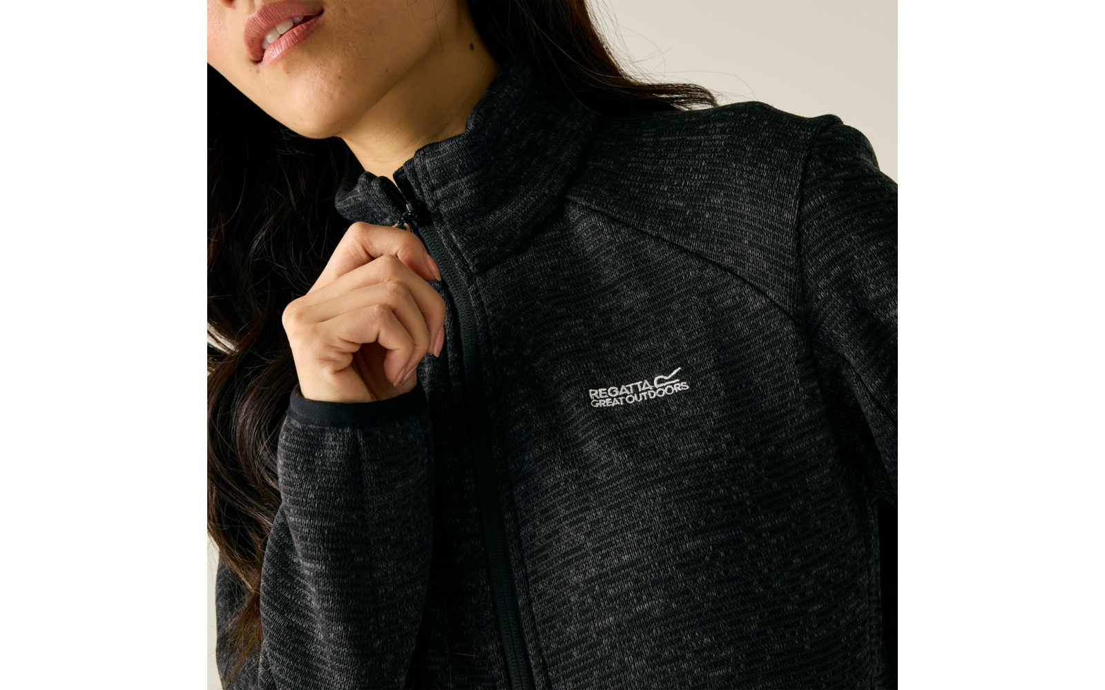 Person von Kinn bis Brust, Hand zieht Reißverschluss einer schwarzen, melierten Fleecejacke mit hohem Kragen und sichtbarem "Regatta Great Outdoors"-Logo auf der linken Brust