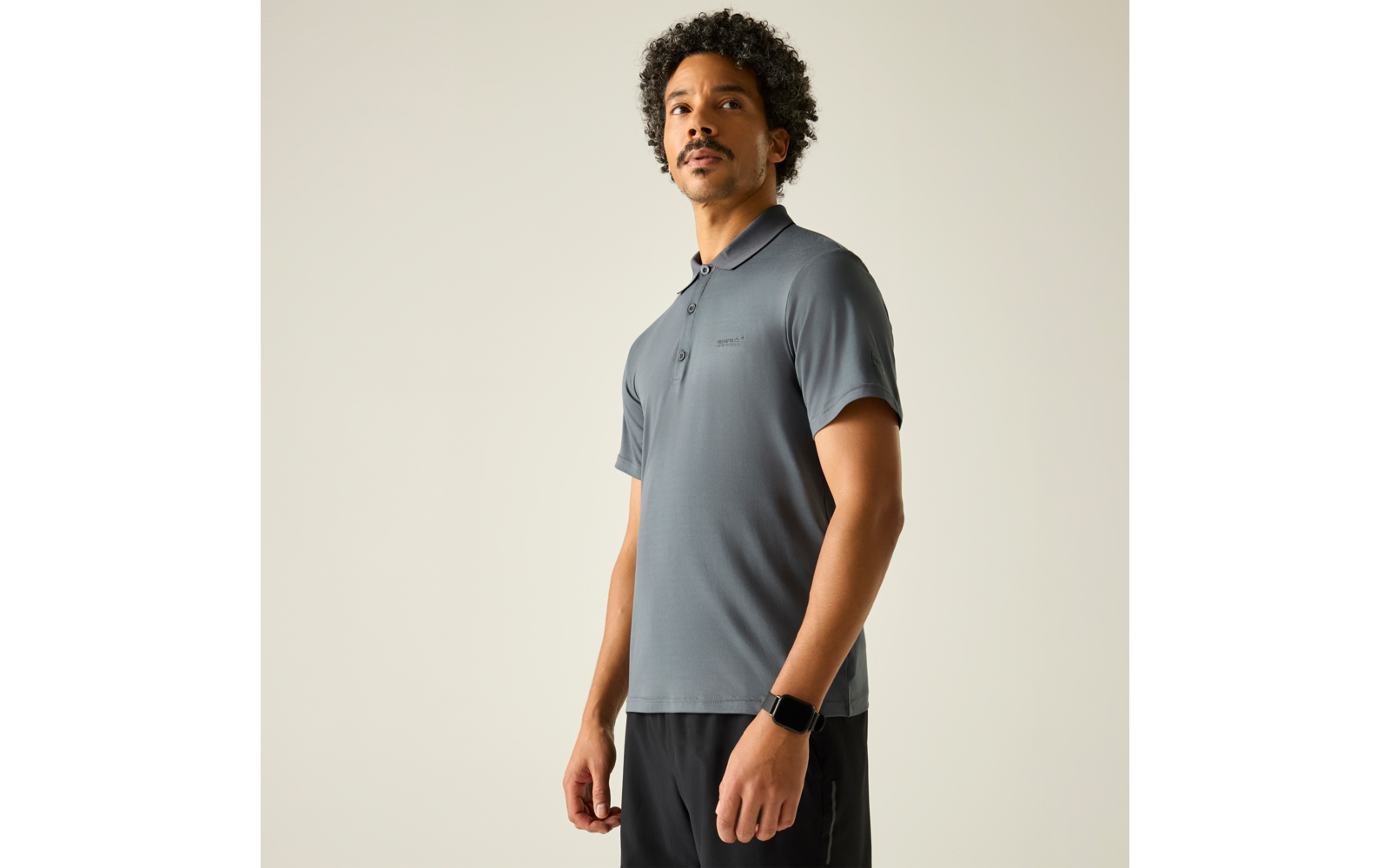 Mann in grauem Poloshirt und schwarzer Hose, trägt Armbanduhr, heller Hintergrund