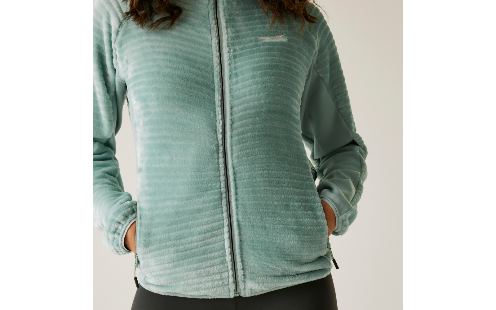 Person trägt eine hellblaue Fleecejacke mit Reißverschluss und hat die Hände in den Taschen