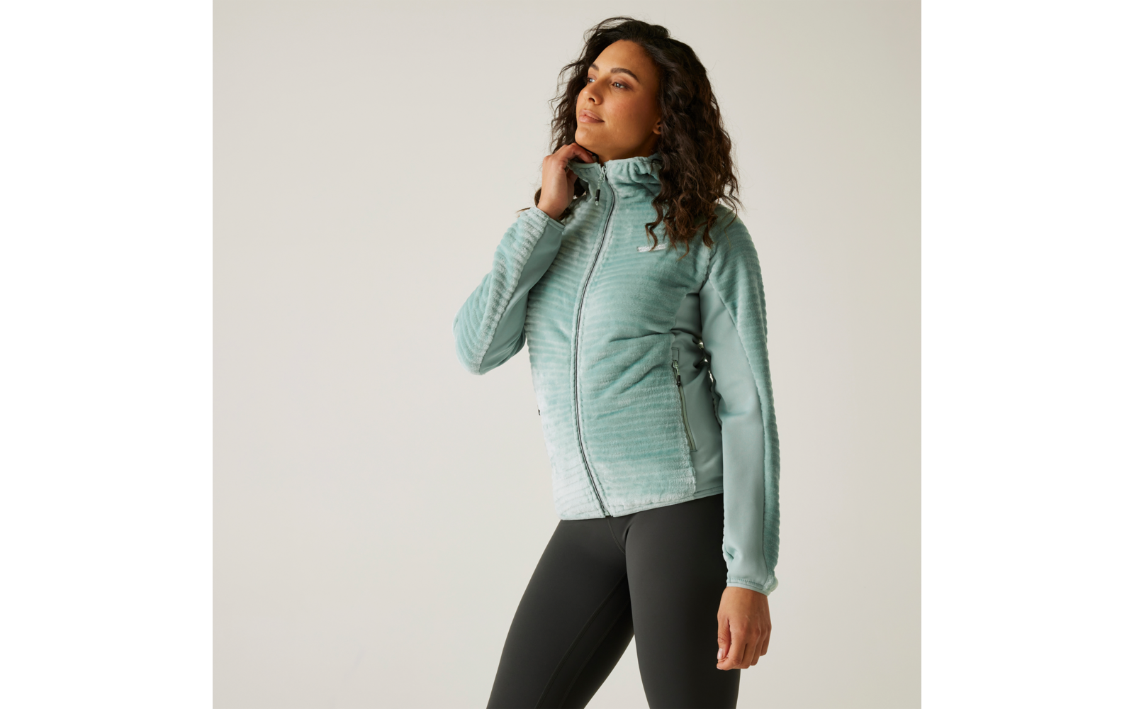 Frau in hellblauer Jacke und schwarzen Leggings vor weißem Hintergrund