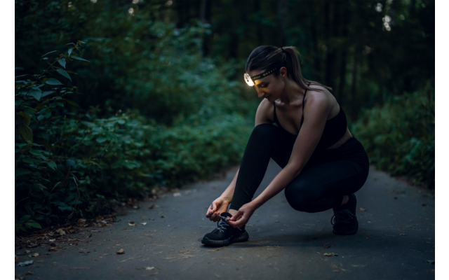 Frau bindet ihre Sportschuhe auf einem Weg im Wald