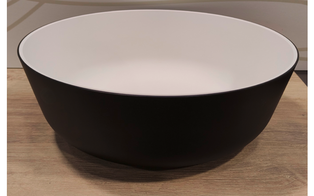 Ronde zwarte kom met witte binnenkant op een houten oppervlak, van voren gefotografeerd