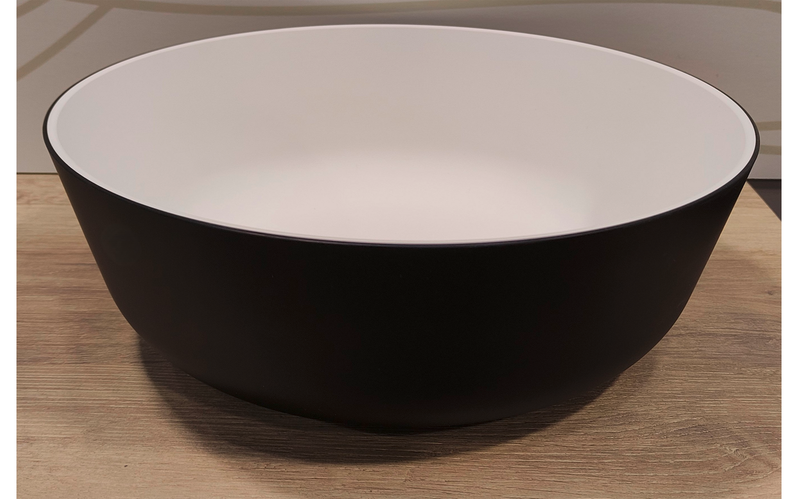 Ronde zwarte kom met witte binnenkant op een houten oppervlak, van voren gefotografeerd