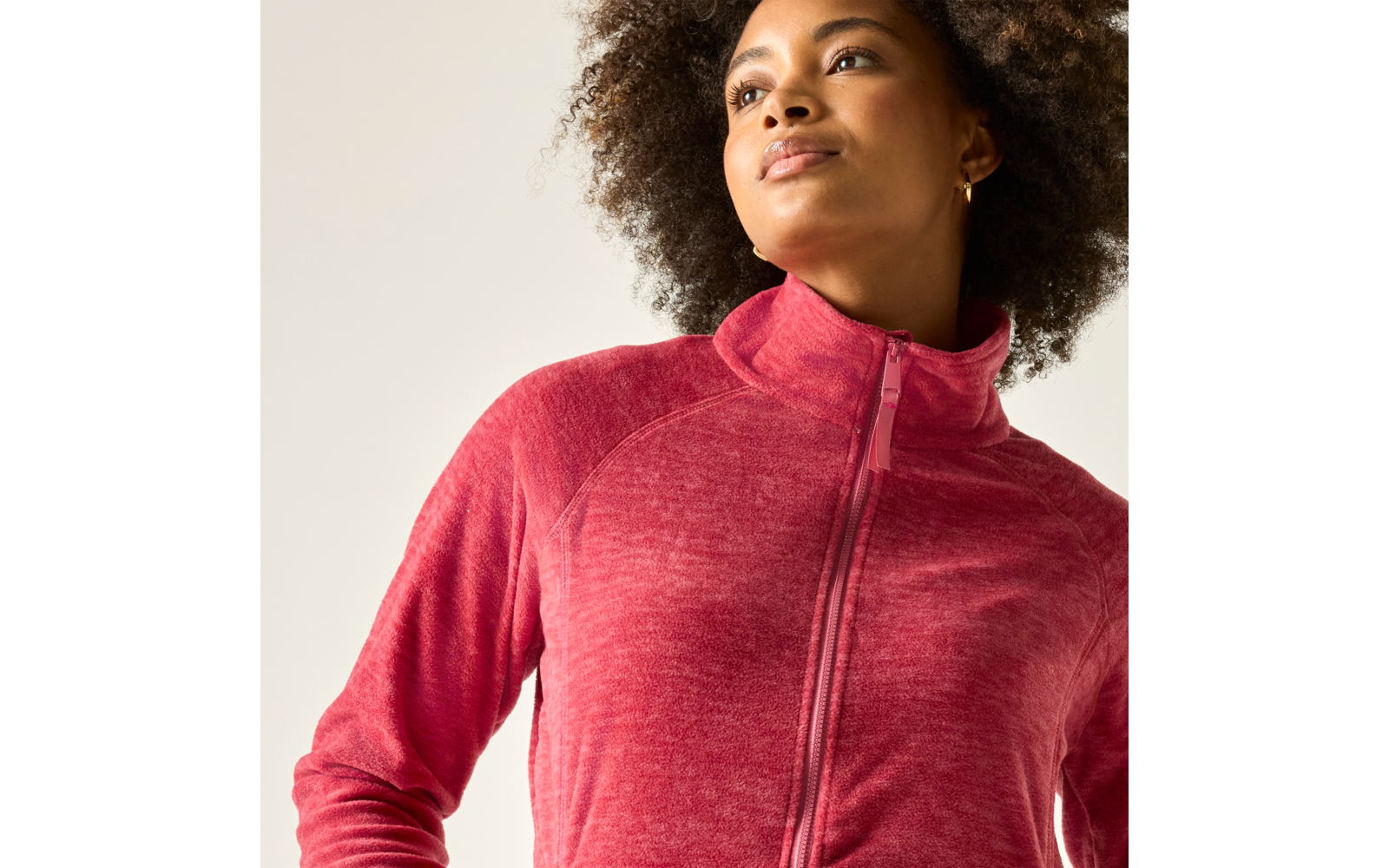 Nahaufnahme einer Frau mit lockigem Haar, die nach oben rechts blickt und eine rote Jacke mit Reißverschluss trägt