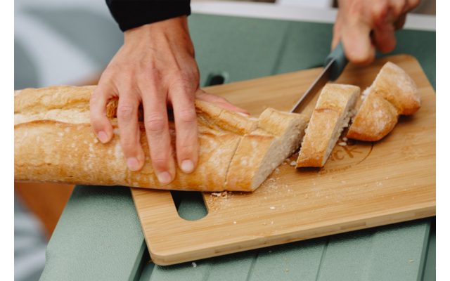 Twee handen snijden een stokbrood met een mes op een houten snijplank
