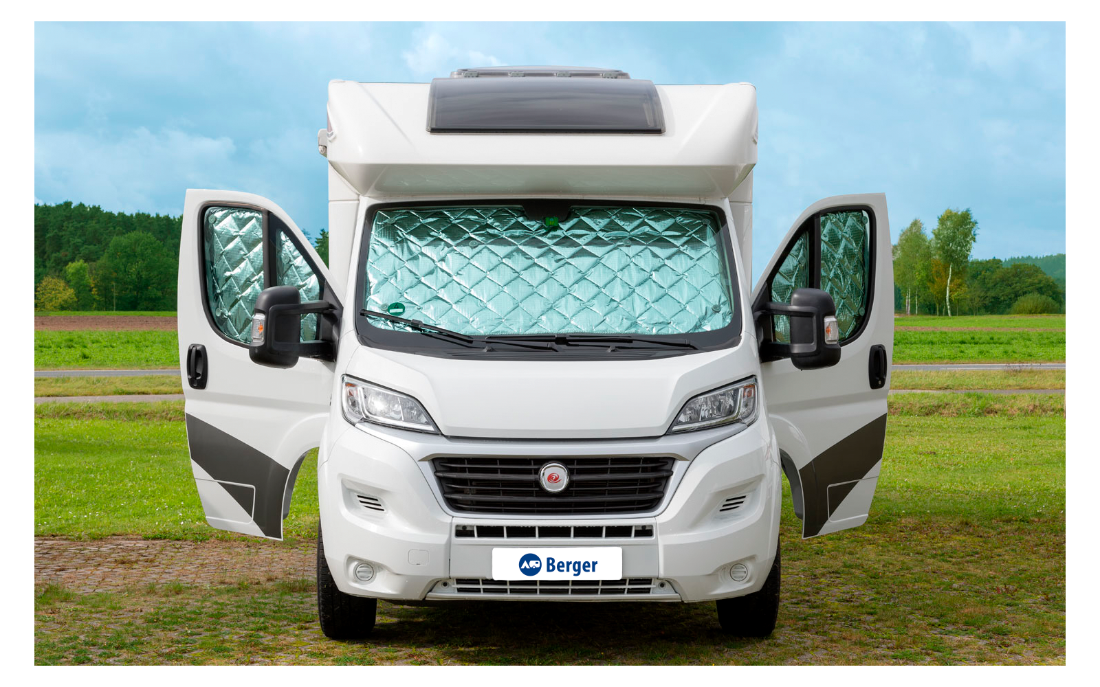 Weißes Wohnmobil mit geöffneten Türen steht auf einem Feldweg vor grünem Wald