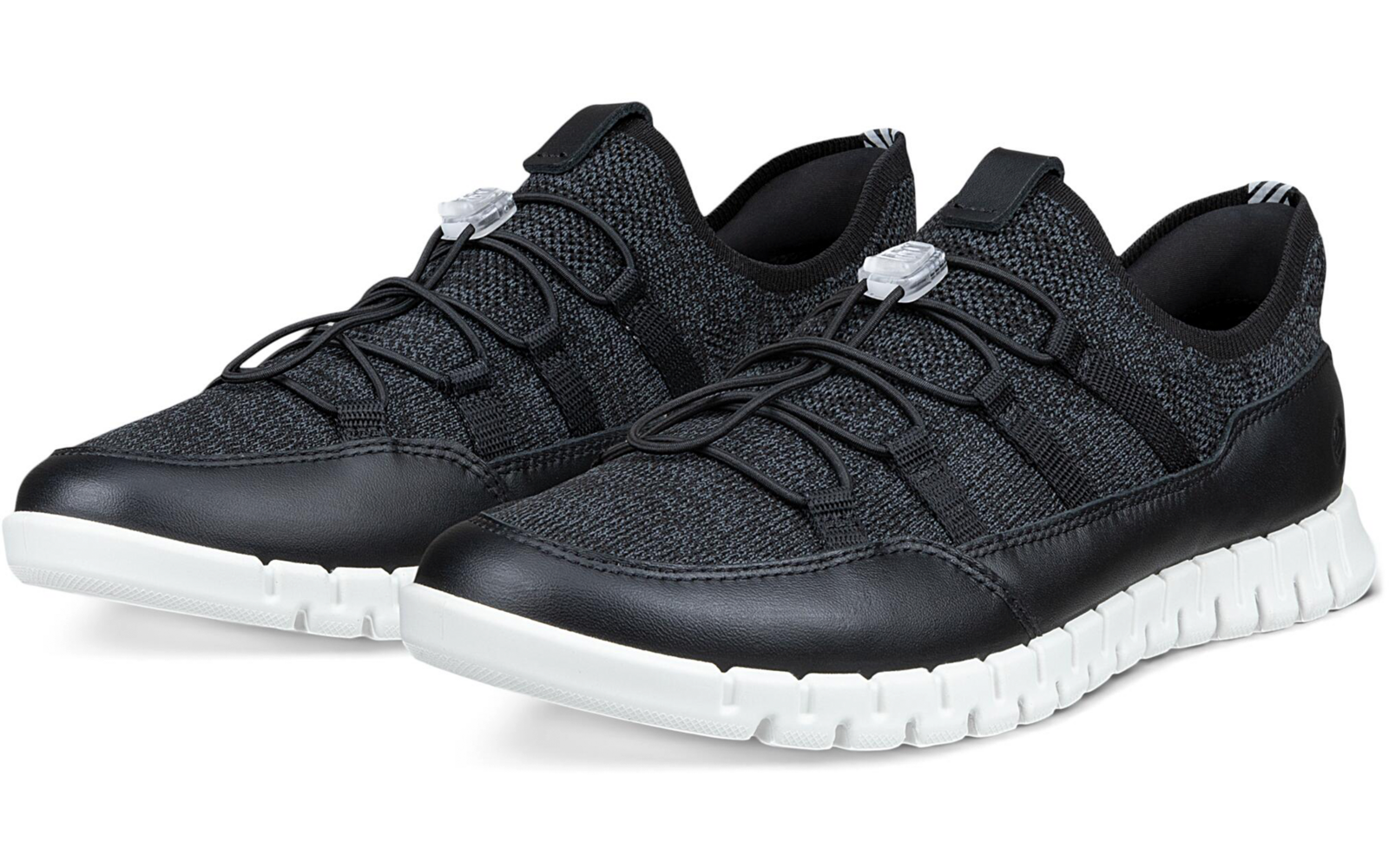 Par de zapatillas negras con parte superior de punto, cordones elásticos con tope y suelas blancas, colocadas inclinadas una junto a la otra sobre fondo blanco