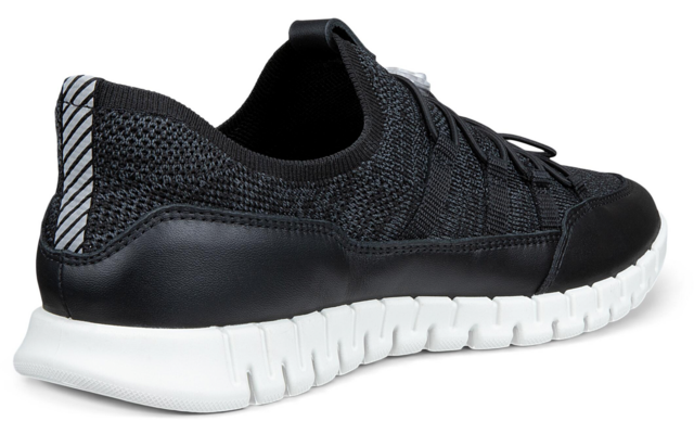 Zapatilla negra en vista lateral/trasera, empeine de punto, cordones negros, suela blanca segmentada, tirador del talón con franjas reflectantes