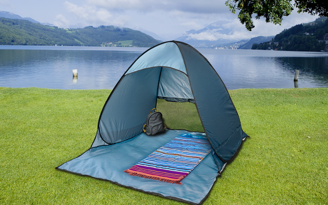 Tente bleue ouverte sur l'herbe, à l'intérieur un tapis rayé et un sac à dos gris