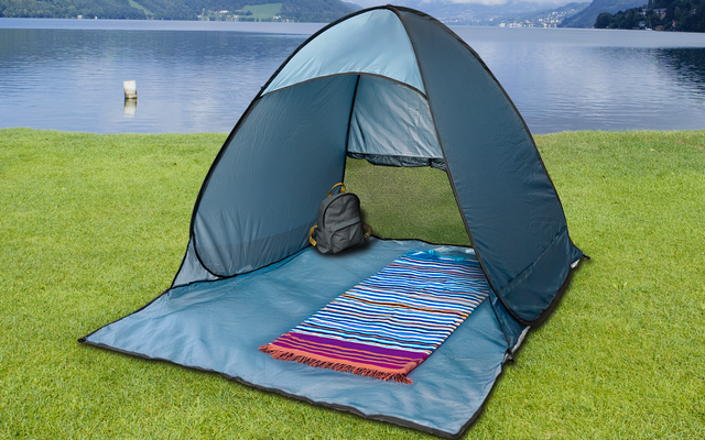 Tenda blu aperta sull'erba, all'interno un tappetino a righe e uno zaino grigio