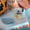 Hand gießt Flüssigkeit aus einem Glas auf einen Untersetzer in Blattform auf einem Tisch
