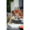 Hand houdt een glas met roze drank boven een tafel met glazen en documenten
